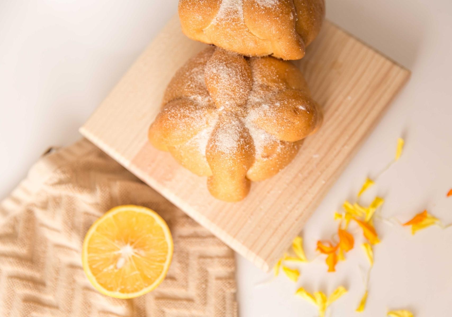 Pan de muerto sobre una tabla de madera de cocina, acompañado de naranja y flor de cempasúchil