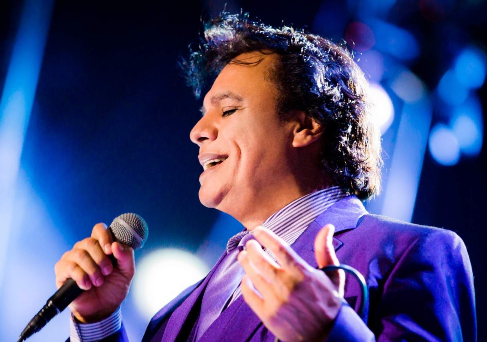 Juan Gabriel de perfil con un traje morado, cantando con un micrófono
