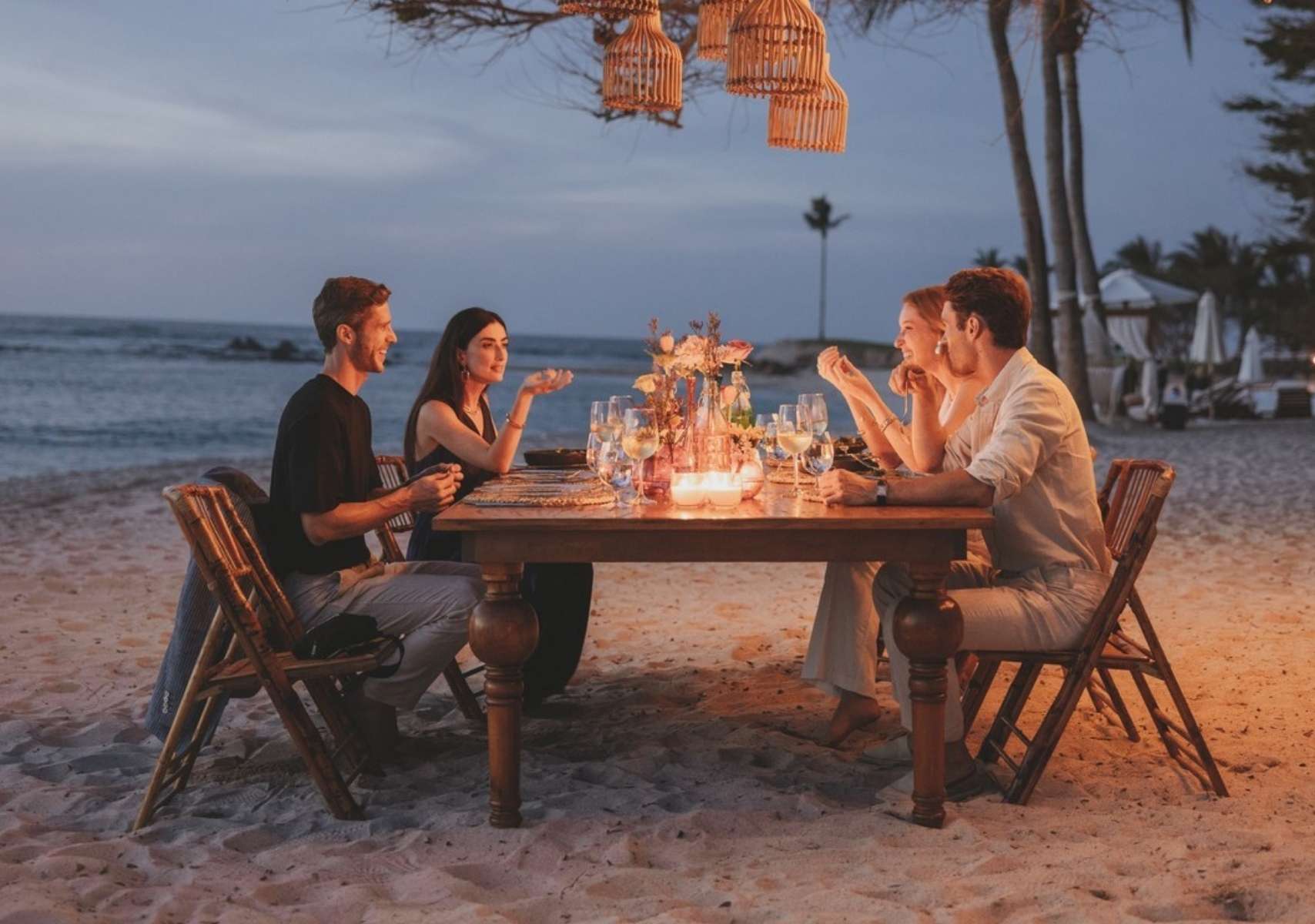 Grupo de amigos cenando en Navidad en Punta Mita, frente al mar, en una mesa sobre la playa